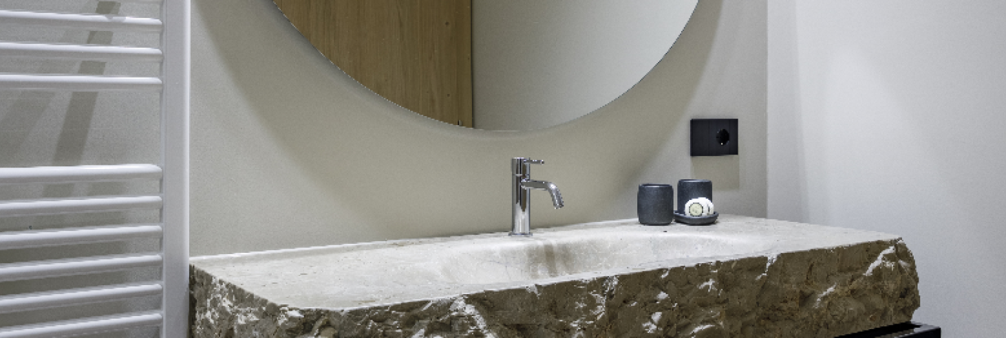 Badezimmer Dolomit Stylisches Badezimmer im Boutique Hotel Sole im Zentrum von Sterzing mit Naturstein-Waschbecken aus Dolomitgestein, modernem Wasserhahn und rundem Spiegel.