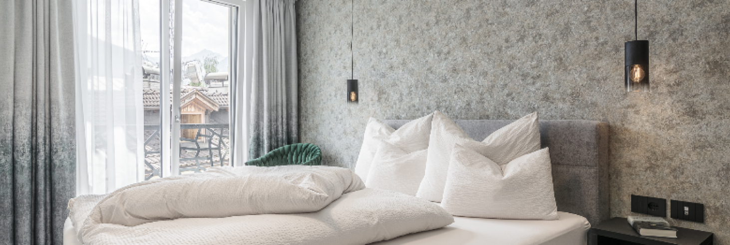 Schlafzimmer Apartment Gneis Schlafzimmer des Apartments Gneis im Boutique Hotel Sole mit gemütlichem Doppelbett, modernen Hängelampen, stilvoller Tapete und Französichem Balkon..