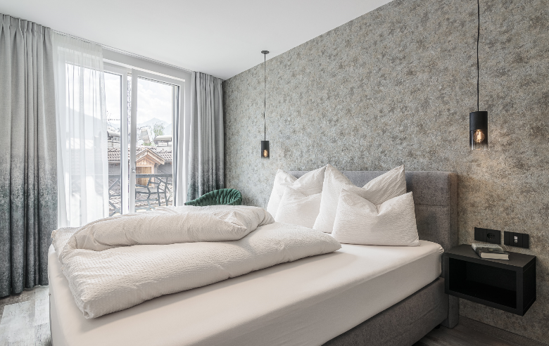 Schlafzimmer Apartment Gneis Schlafzimmer des Apartments Gneis im Boutique Hotel Sole mit gemütlichem Doppelbett, modernen Hängelampen, stilvoller Tapete und Französichem Balkon..