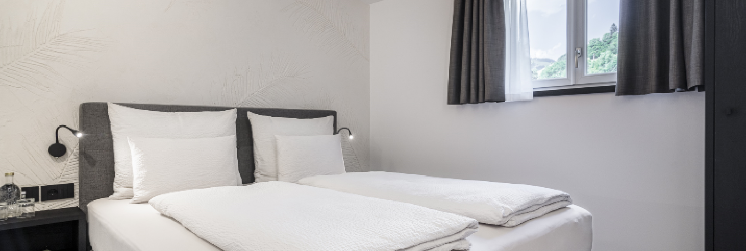 Schlafzimmer im Hotel Sole Modern eingerichtetes Hotelzimmer im Boutique Hotel Sole in Sterzing mit gemütlichem Doppelbett, stilvollem Dekor und Blick auf die Berge durch das Fenster.