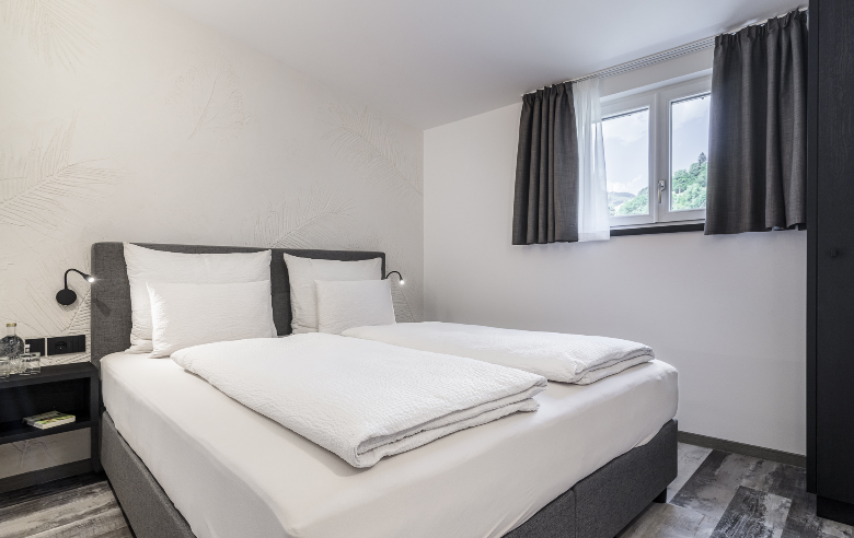 Schlafzimmer im Hotel Sole Modern eingerichtetes Hotelzimmer im Boutique Hotel Sole in Sterzing mit gemütlichem Doppelbett, stilvollem Dekor und Blick auf die Berge durch das Fenster.