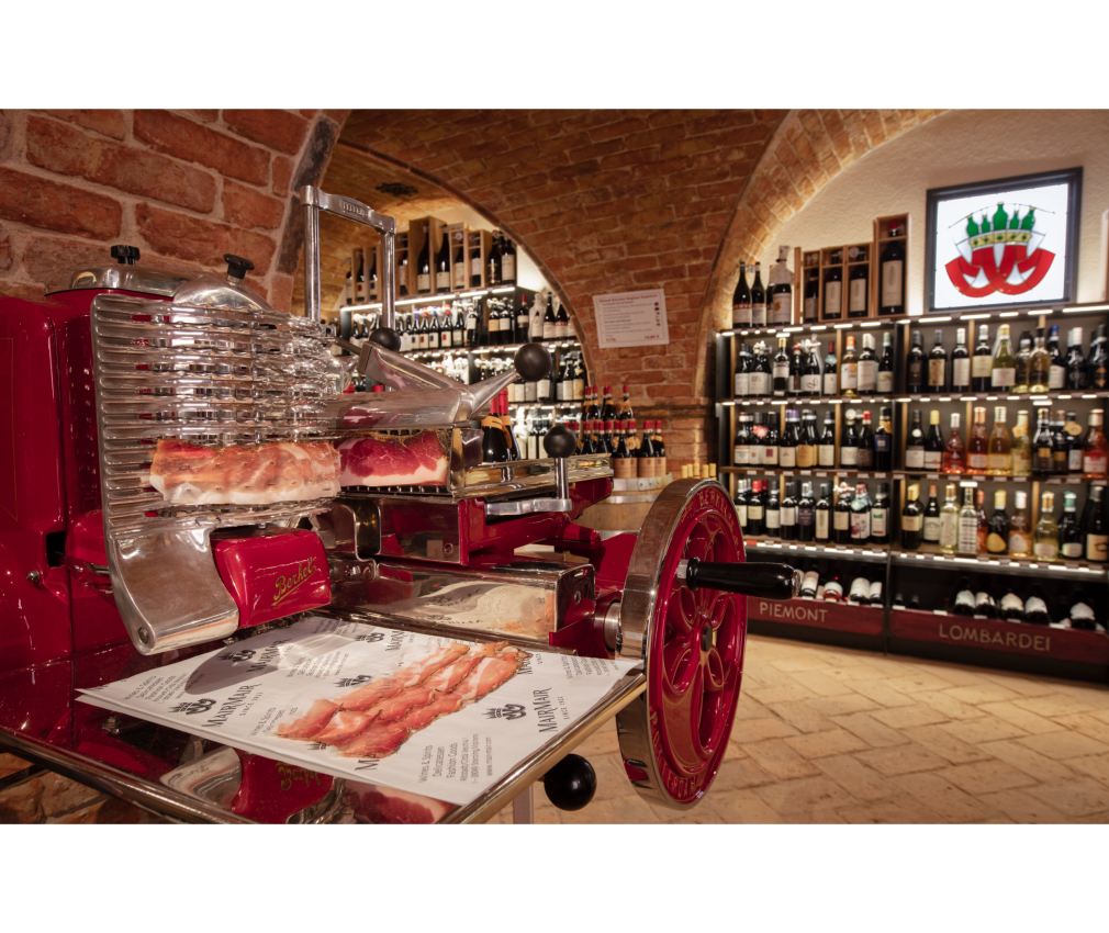 Berkel im Mair Mair Weinkeller Klassische Berkel-Schneidemaschine in der Enoteca von Mair Mair, umgeben von Backsteinwänden und edel beleuchteten Weinregalen.