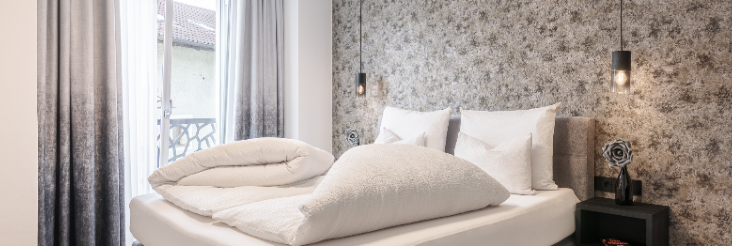 Schlafzimmer Gneis Hotel Sole Schlafzimmer des Apartments Gneis im Boutique Hotel Sole mit stilvollem Design, gemütlichem Doppelbett, moderner Tapete, Hängelampen und bodentiefen Fenstern.