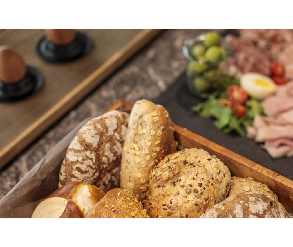 Brotauswahl im Hotel Sole Frische Brötchen und Brot in einer Holzschale, dazu ein Frühstücksbuffet mit Oliven, Aufschnitt, Ei und Tomaten im Hintergrund im Boutique Hotel Sole