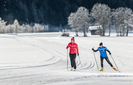 Langlaufen in Pfitsch Zwei Langläufer auf einer verschneiten Loipe, umgeben von winterlicher Landschaft mit frostbedeckten Bäumen und einer kleinen Hütte. Pfitsch bei Stering