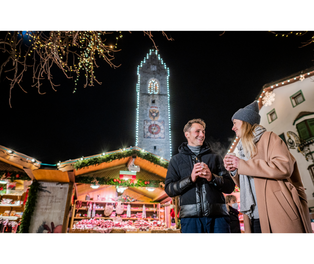 Weihnachtsmarkt in Sterzing Aufnahme im Zentrum von Sterzing vor dem Zwölferturm. Ein Paar genießt den Weihnachtsmarkt mit dampfenden Tassen in festlicher, winterlicher Atmosphäre.