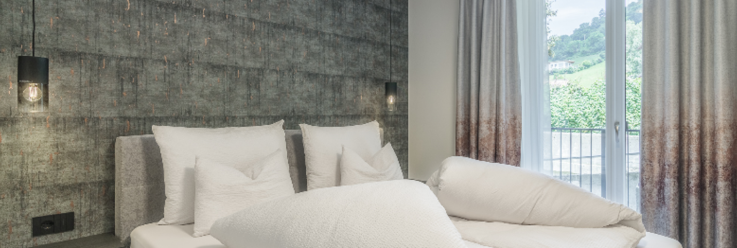 Schlafzimmer Porphyr Hotel Sole Modernes Schlafzimmer im Boutique Hotel Sole mit stilvoller Akzentwand, gemütlichem Doppelbett und Balkon mit Blick auf die grüne Hügellandschaft.