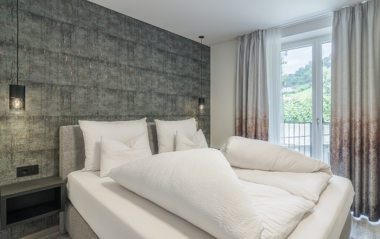 Schlafzimmer Porphyr Hotel Sole Modernes Schlafzimmer im Boutique Hotel Sole mit stilvoller Akzentwand, gemütlichem Doppelbett und Balkon mit Blick auf die grüne Hügellandschaft.