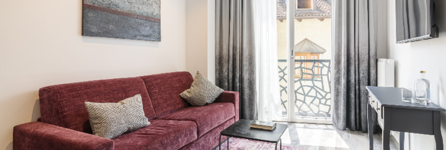 Wohnbereich Apartment Gneis Wohnbereich des Apartments Gneis im Boutique Hotel Sole mit modernem Design, weinrotem Sofa, stilvollen Kissen, Wandkunst und bodentiefen Fenstern.