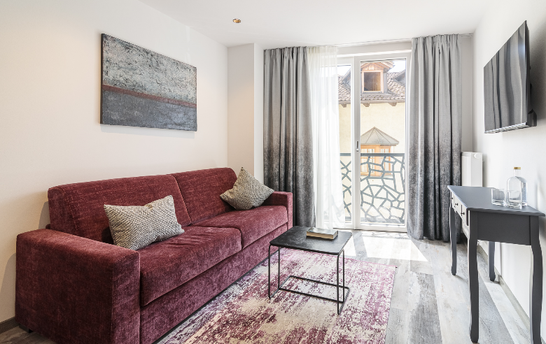 Wohnbereich Apartment Gneis Wohnbereich des Apartments Gneis im Boutique Hotel Sole mit modernem Design, weinrotem Sofa, stilvollen Kissen, Wandkunst und bodentiefen Fenstern.