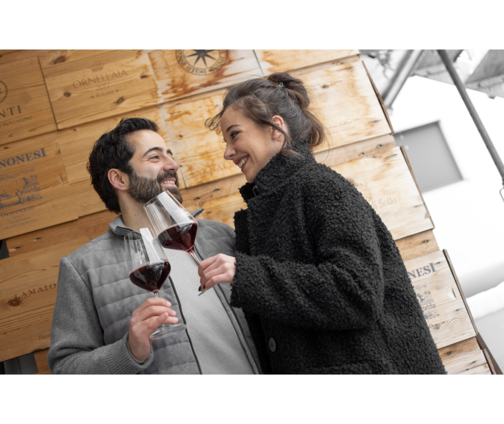 Die Gastgeber im Hotel Sole und Mair Mair Ein herzliches Gastgeberpaar des Hotel Sole genießt ein Glas Rotwein vor einer rustikalen Wand aus edlen Weinkisten und strahlt pure Gastfreundschaft aus.