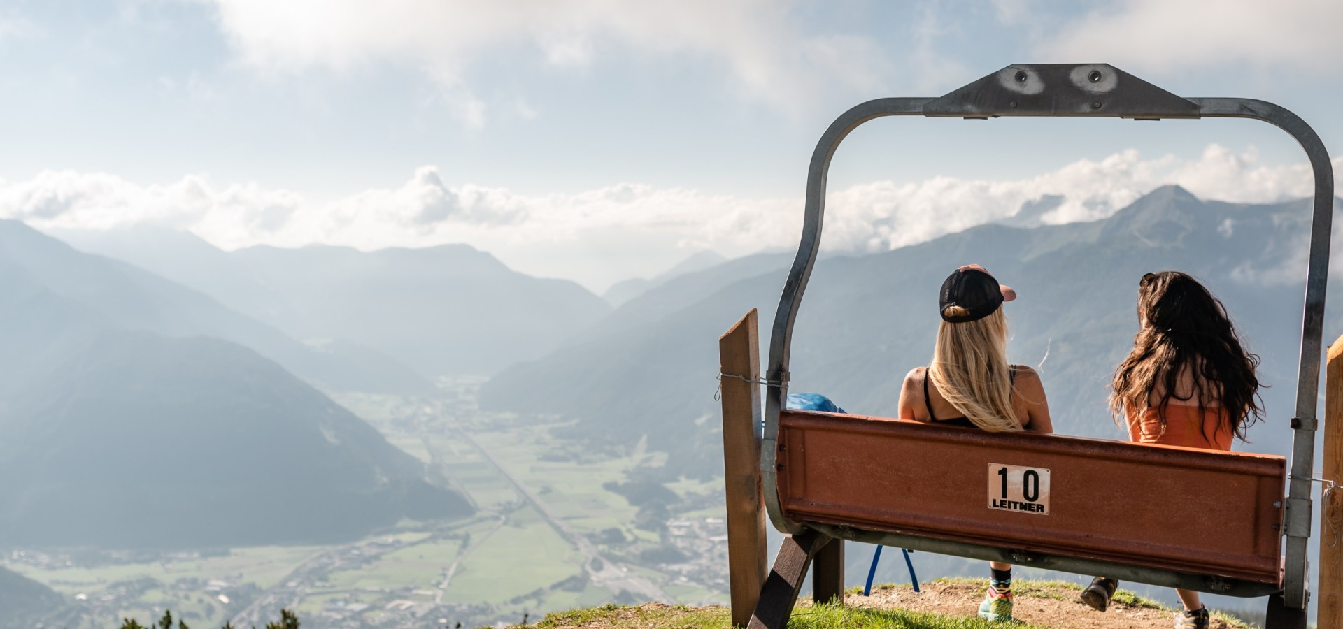 Bergblick vom Rosskopf Zwei Frauen sitzen auf einer umgebauten Skilift-Bank und genießen den Panoramablick auf das Wipptal, Trens, Stilfes und Sterzing vom Berg Rosskopf.