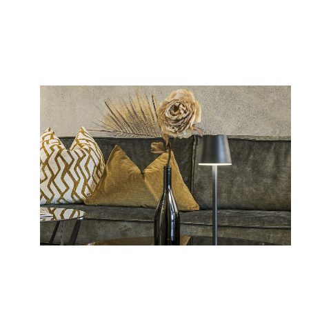 Eingangsbereich Hotel Sole Sitzecke im Hotel Sole mit goldenen Kissen, einer Trockenblume in einer schwarzen Flasche und einer modernen Tischlampe vor einer strukturierten Wand.