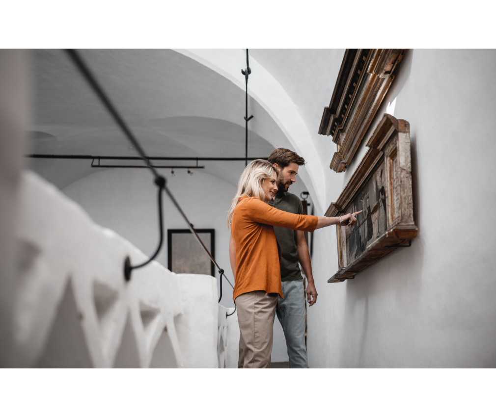 Ausstellung im Rathaus Paar im historischen Rathaus von Sterzing betrachtet interessiert ein altes Gemälde, das in einem kunstvoll verzierten Holzrahmen an der Wand hängt.