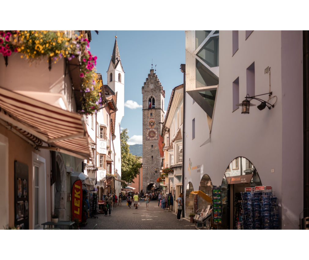 Altstadt Sterzing und Zwölferturm Belebte Altstadt mit Geschäften und dem Zwölferturm als Wahrzeichen von Sterzing, eingerahmt von historischer und moderner Architektur.