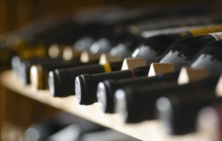 Verschiedene Weinflaschen liegen auf einem Holzregal im Weinkeller vom Geschäft Mair Mair. Der Hintergrund ist verblasst und harmonisch.