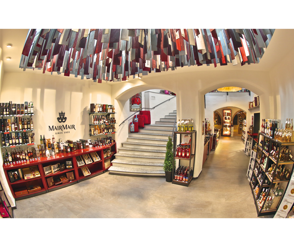 Enothek Mair Mair Edle Enothek Mair Mair in Sterzing mit moderner Deckendekoration, stilvoll beleuchtetem Innenraum und einer Treppe, die in den oberen Bereich führt.