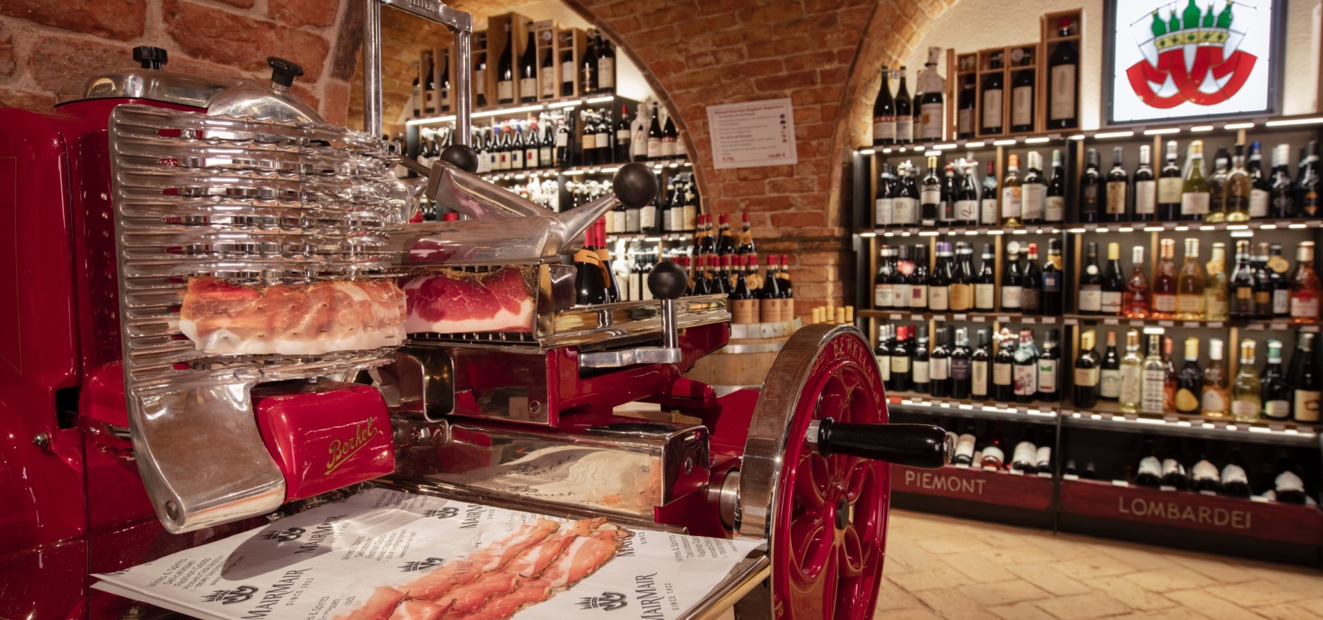 Affettatrice vintage e selezione di vini da Mair Mair Affettatrice Berkel rossa in un'enoteca con soffitto a volta in mattoni, circondata da una raffinata selezione di vini italiani.