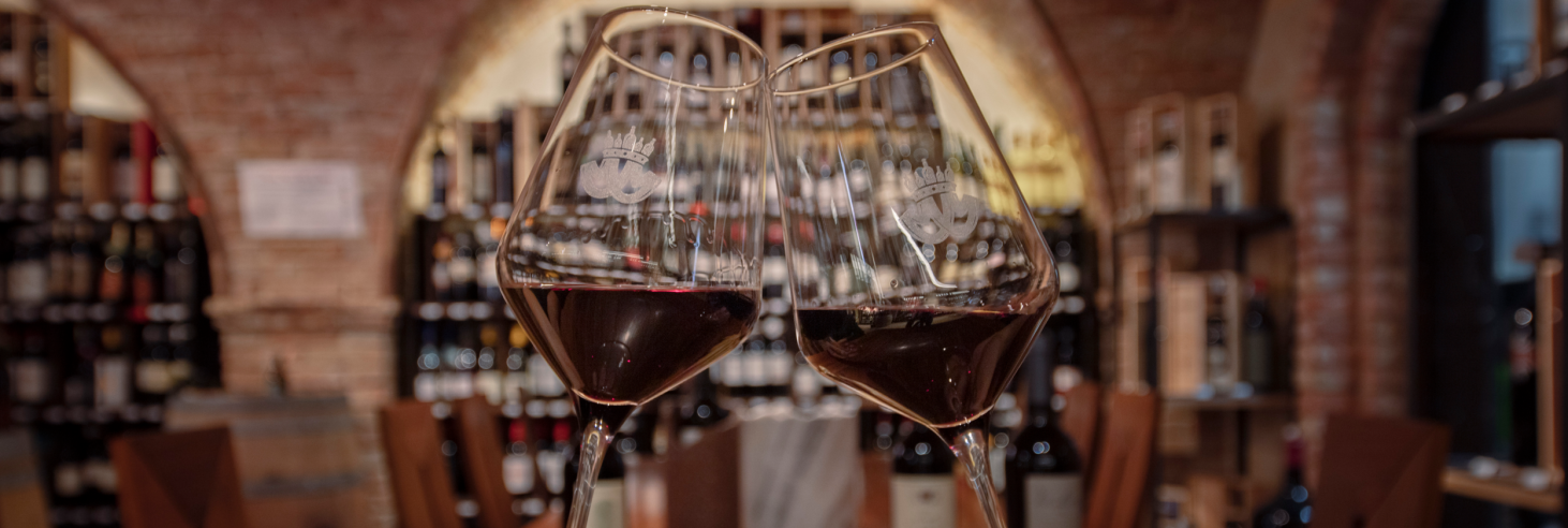 Mair Mair Enothek Zwei Rotweingläser in einem stimmungsvollen Weinkeller mit Backsteinwänden und Weinregalen. Weinverkostung und Genuss in Südtirol. Mair Mair Enothek