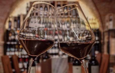 Zwei Rotweingläser in einem stimmungsvollen Weinkeller mit Backsteinwänden und Weinregalen. Weinverkostung und Genuss in Südtirol. Mair Mair Enothek