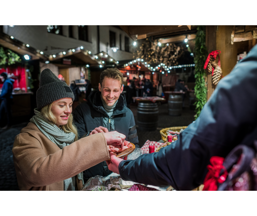 Paar genießt regionale Spezialitäten auf dem Weihnachtsmarkt in Sterzing. Gemütliche Winterstimmung mit Lichtern und Holzhütten in Südtirol.