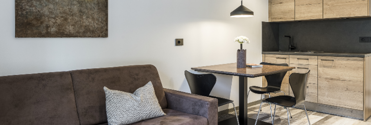 Wohnraum Porphyr Hotel Sole Stilvolles Apartment im Boutique Hotel Sole mit braunem Sofa, modernem Essbereich und offener Holzküche, harmonisch gestaltet mit warmen Farbtönen.