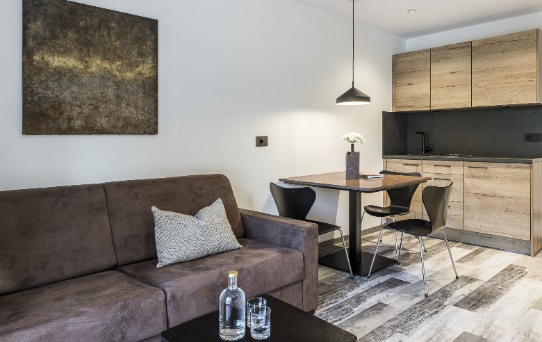 Wohnraum Porphyr Hotel Sole Stilvolles Apartment im Boutique Hotel Sole mit braunem Sofa, modernem Essbereich und offener Holzküche, harmonisch gestaltet mit warmen Farbtönen.