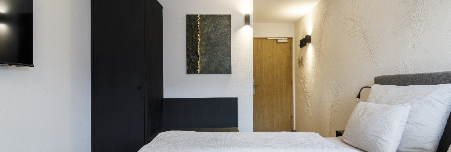 Zimmer im Boutique Hotel Sole Modern eingerichtetes Hotelzimmer mit einem großen, gemütlichen Bett, stilvollen dunklen Möbeln und stimmungsvollem Licht für eine entspannte Atmosphäre.