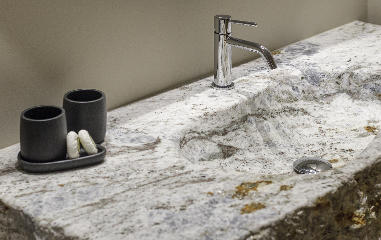 Waschbecken Plima im Hotel Sole Waschbecken aus hellem Naturstein mit einzigartiger Maserung im Boutique Hotel Sole, ergänzt durch eine moderne Armatur und stilvolle schwarze Accessoires.