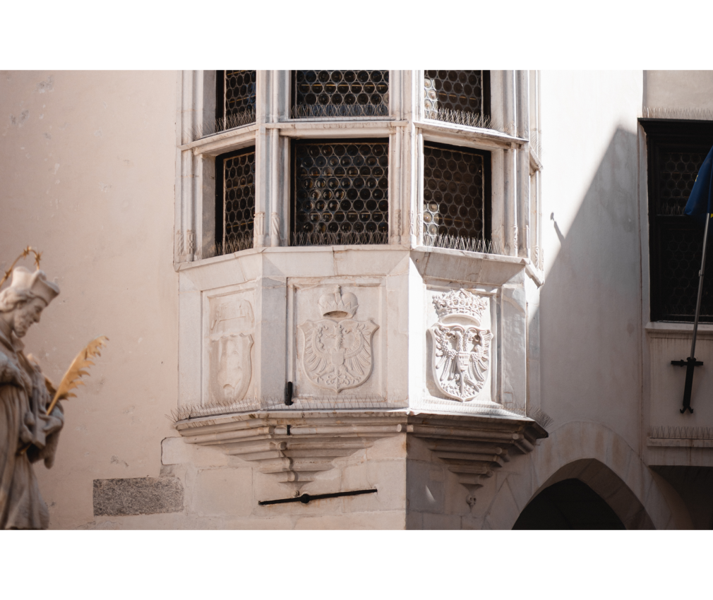 Erker am Rathaus Historischer Erker am Rathaus von Sterzing mit verzierten Wappen, filigranen Gittern und einer Nepomukstatue im Vordergrund.