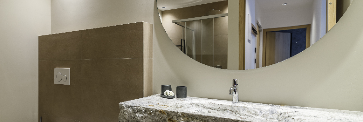 Badezimmer Apartment Plima Elegantes Badezimmer im Boutique Hotel Sole mit Naturstein-Waschbecken, großer Spiegelwand, moderner Dusche und stilvollen Armaturen für höchsten Komfort.
