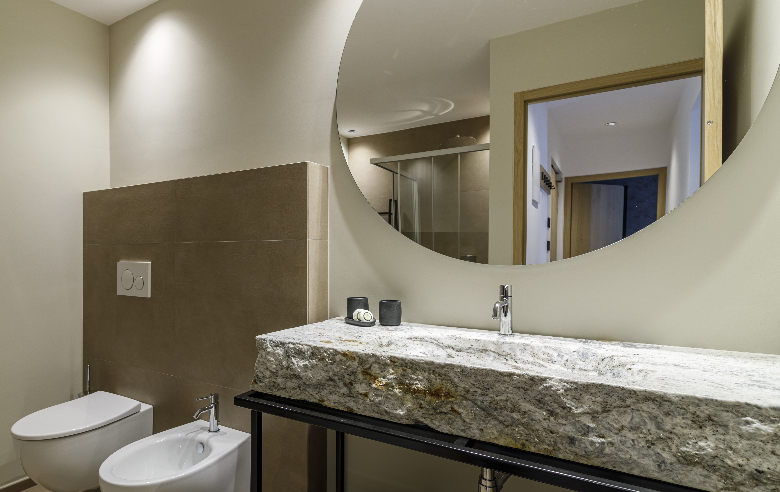 Badezimmer Apartment Plima Elegantes Badezimmer im Boutique Hotel Sole mit Naturstein-Waschbecken, großer Spiegelwand, moderner Dusche und stilvollen Armaturen für höchsten Komfort.