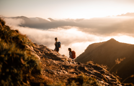 Sonnenaufgang am Rosskopf Zwei Wanderer steigen bei Sonnenaufgang einen felsigen Bergpfad hinauf, umgeben von Wolken und einer atemberaubenden Berglandschaft in Südtirol